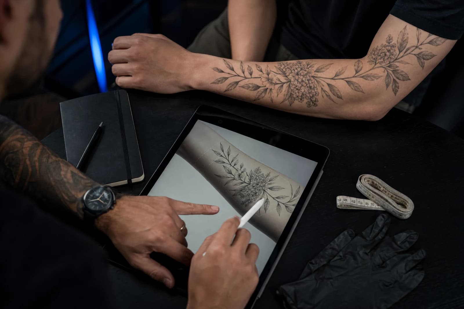 A tattoo artist and client reviewing a forearm placement on a tablet